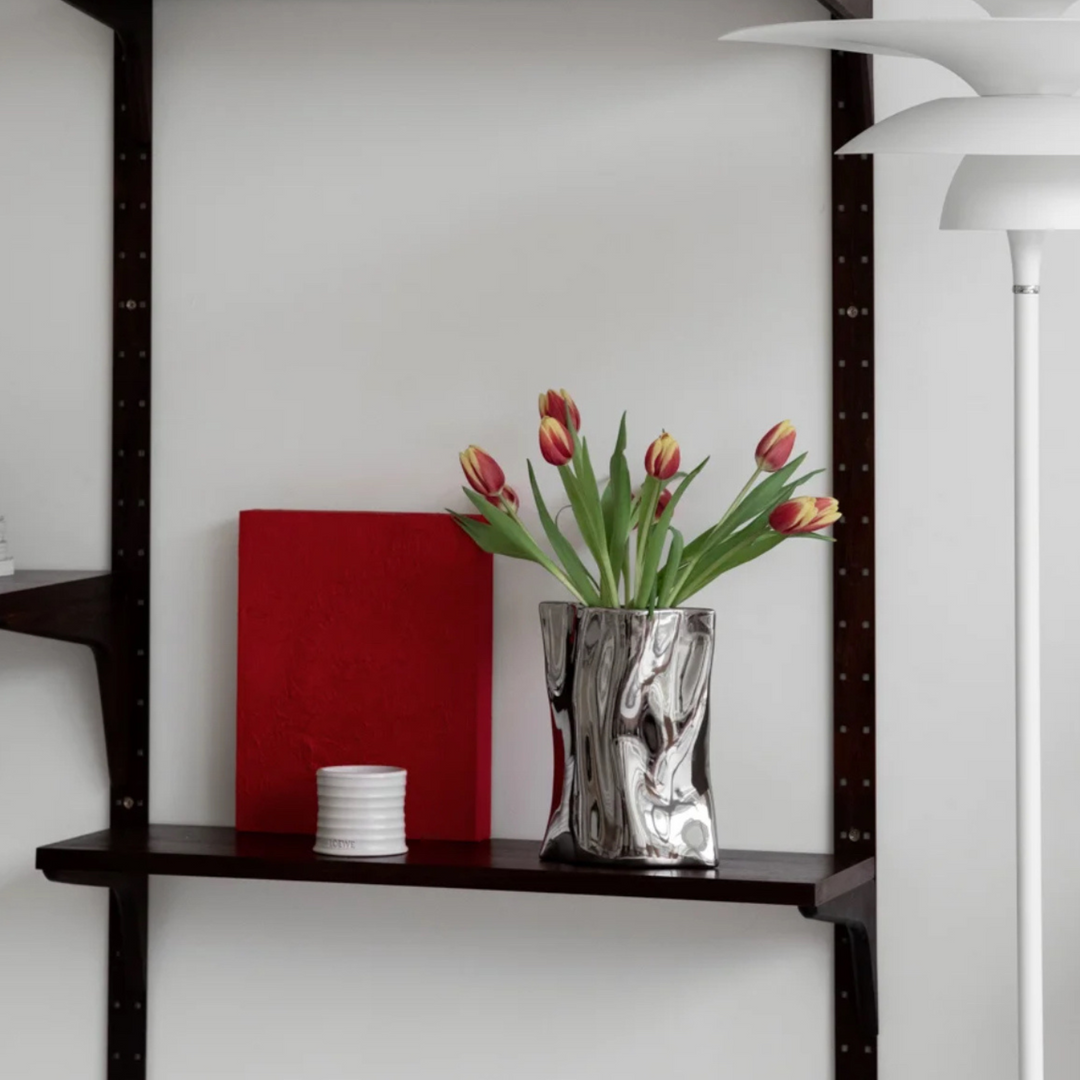 Reflective silver vase styled with tulips and bold accents on a contemporary shelf.