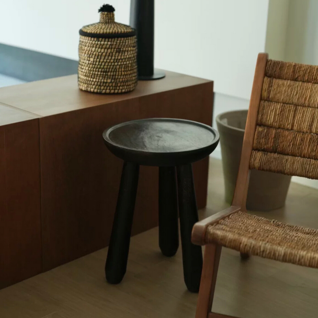 Rustic dark wooden side table placed next to a woven chair, adding a natural aesthetic to the living room.