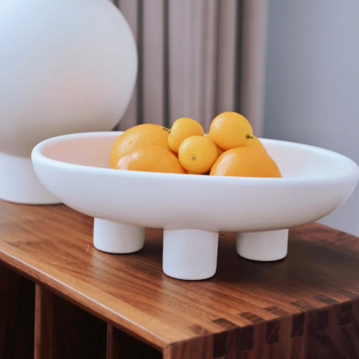 White fruit bowl with oranges, elevated on distinctive raised legs. Ideal for Scandinavian-inspired kitchens or living spaces.