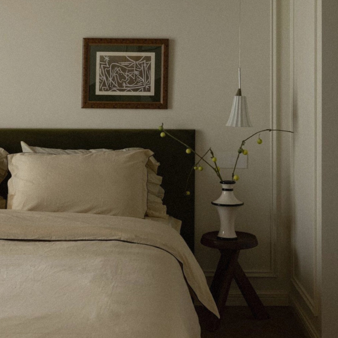 sculptural ceramic vase with delicate branches placed on a bedside table in a soft neutral bedroom interior.