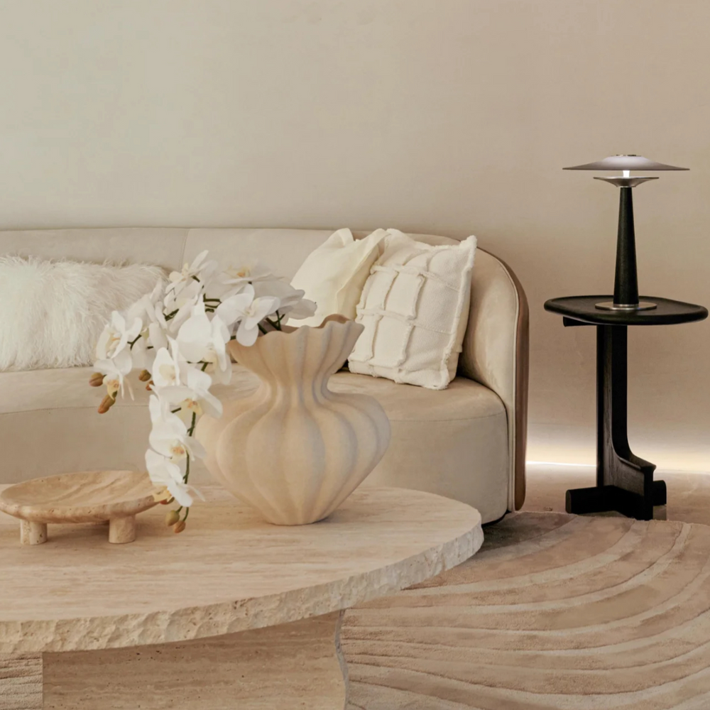 Sculptural ceramic vase with flowing curves on a travertine table in a modern minimalist living room.