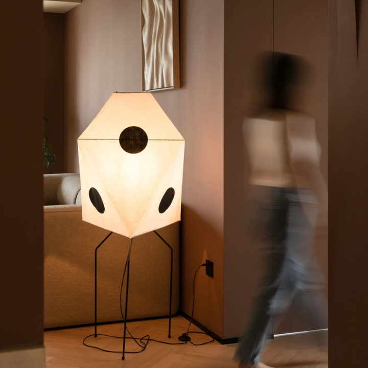 A bold geometric floor lamp positioned in a modern room with clean lines and soft brown tones.