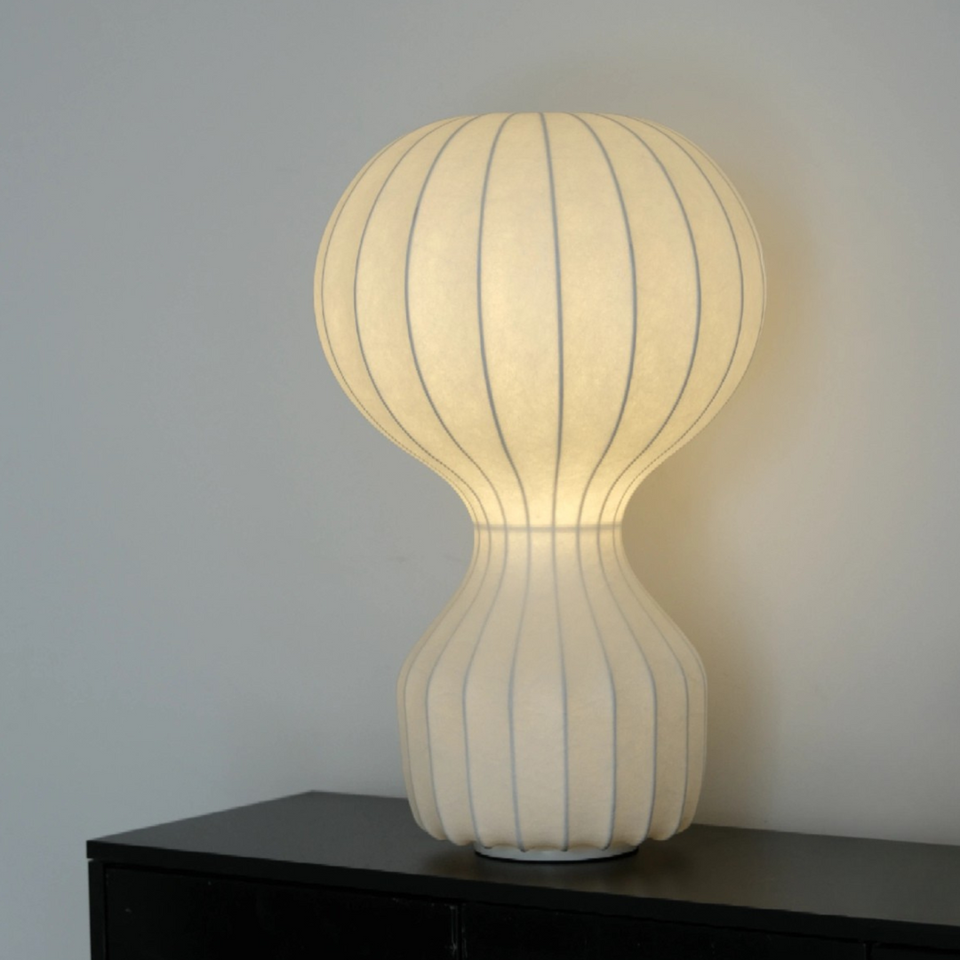 Artistic table lamp glowing warmly in a soft minimalist setting.