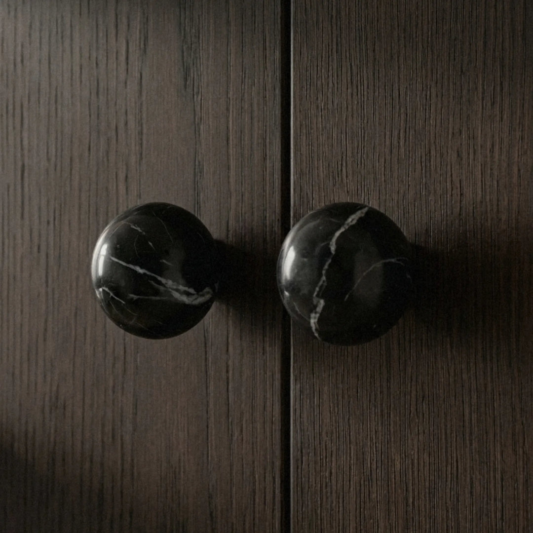 Sculptural black stone cabinet knobs on dark wood cabinet in minimalist organic modern interior.