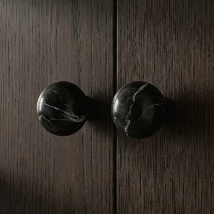 Sculptural black stone cabinet knobs on dark wood cabinet in minimalist organic modern interior.