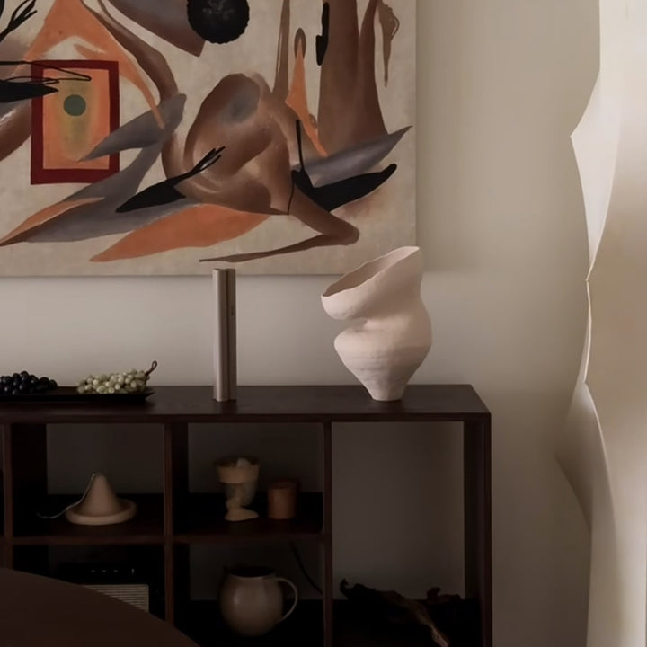 Sculptural vase placed near lamp in an earthy modern living room.