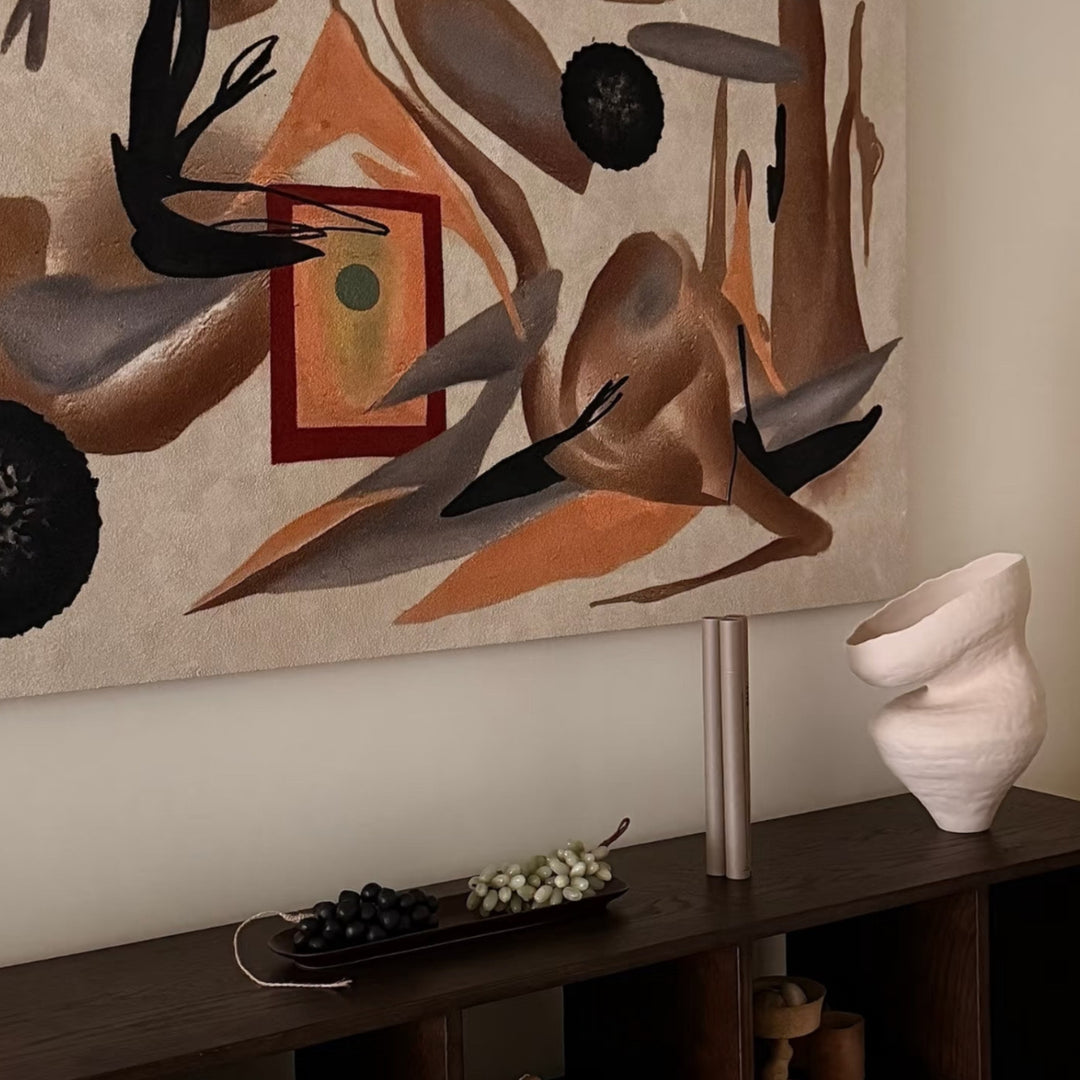 Sculptural vase styled on a dark wood cabinet under abstract wall art.