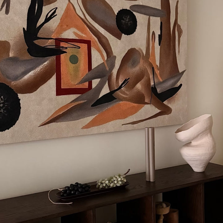 Sculptural vase styled on a dark wood cabinet under abstract wall art.
