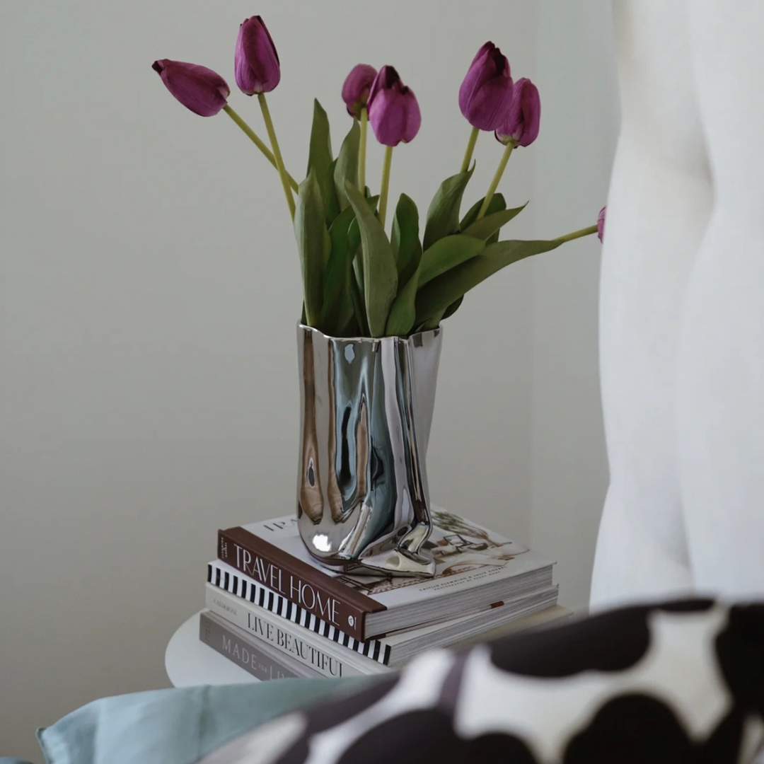 A silver metallic vase filled with tulips on a stack of books, perfect for modern minimalist home decor.