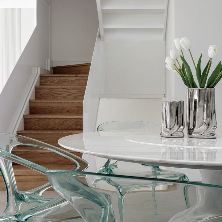 Sleek silver vase holding white tulips, styled on a modern round dining table with glass chairs.