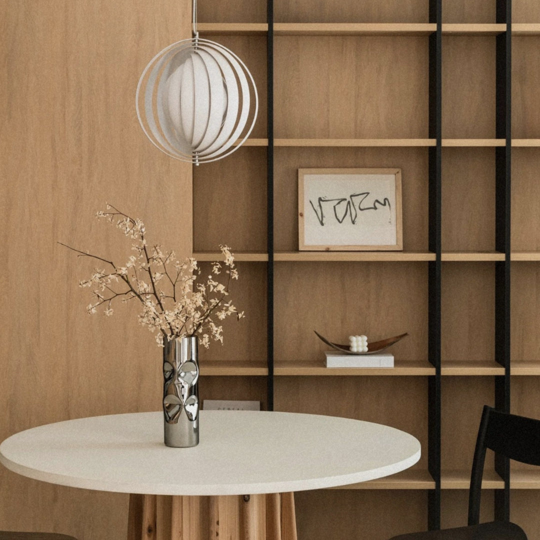 slatted pendant light hanging above a round dining table in a wood interior.