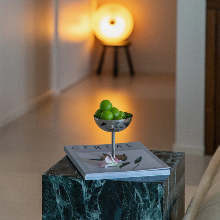 Sleek stainless steel coupe filled with fresh green grapes, placed on a marble table in a contemporary living space.