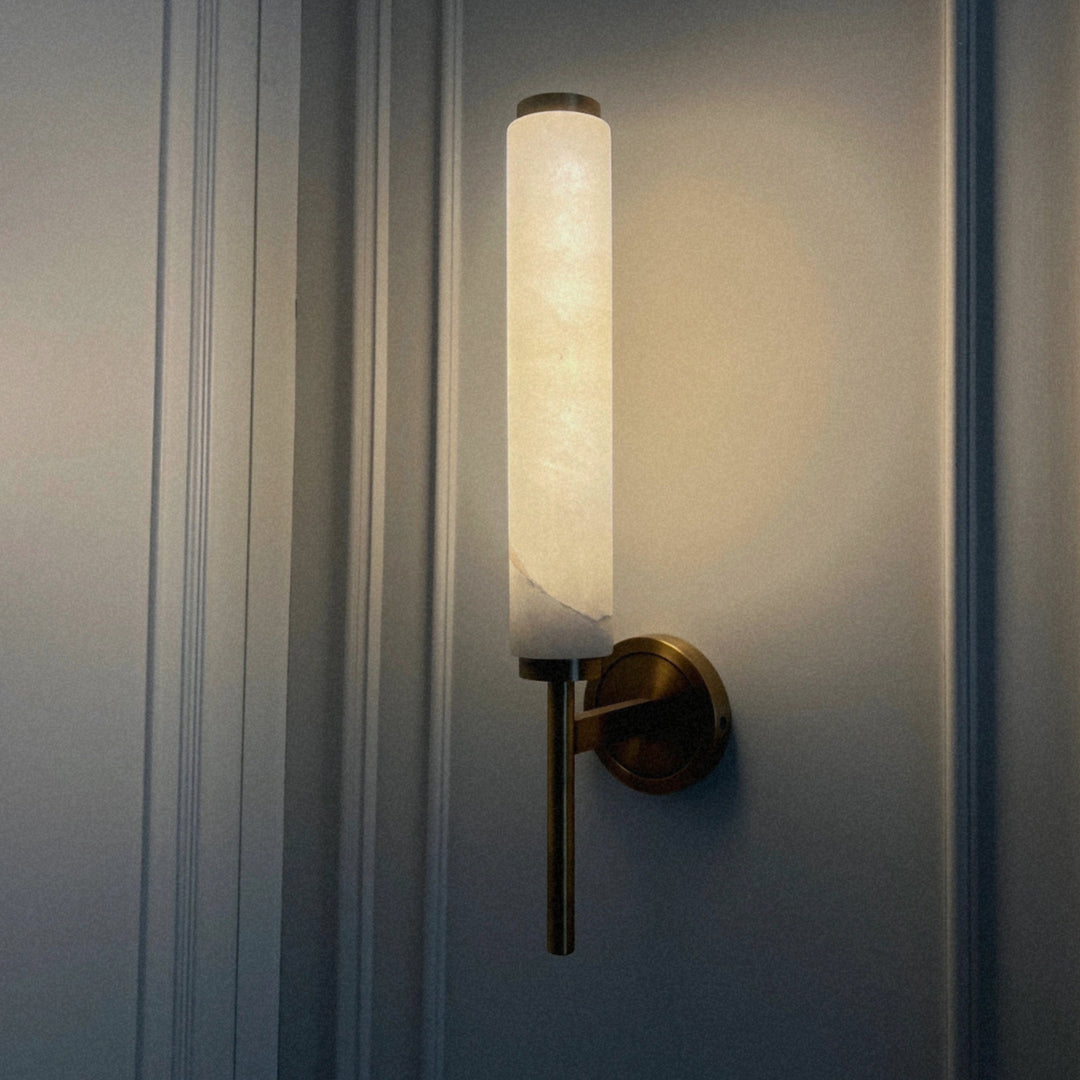 spanish marble wall light with brass base casting a warm glow against a paneled wall.