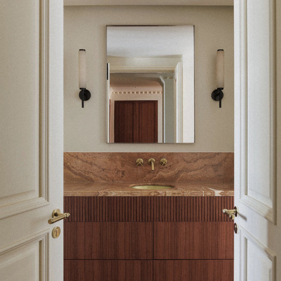 spanish marble wall sconce mounted beside a bathroom mirror creating soft ambient lighting above a marble vanity.