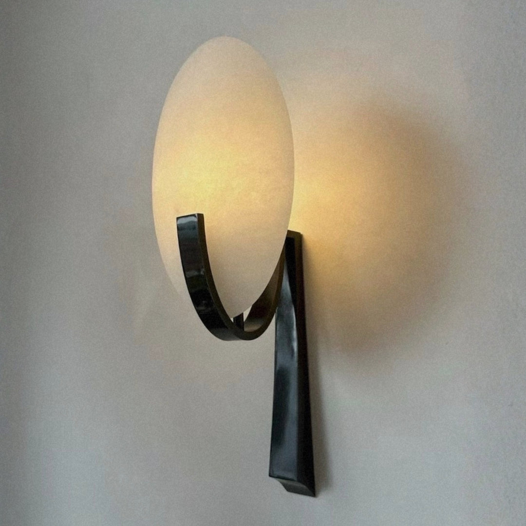 spanish marble wall sconce with an oval stone diffuser mounted on a curved metal arm.
