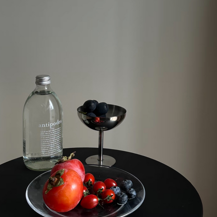 Stylish stainless steel coupe holding fresh fruit, complemented by a sleek water bottle on a dark modern table.