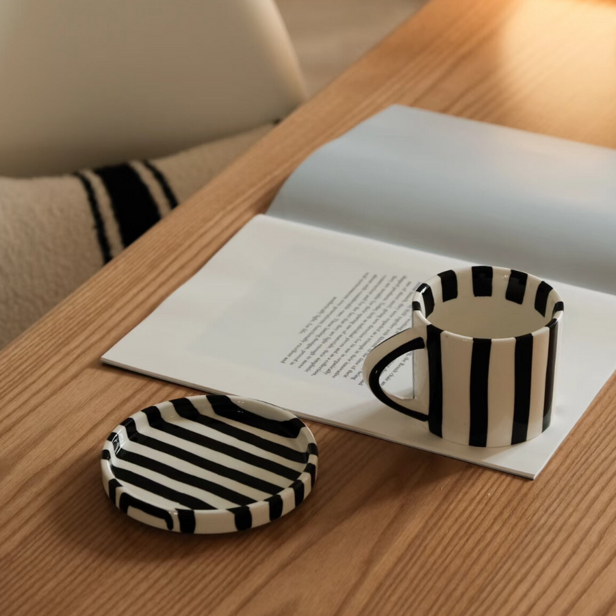 Striped ceramic mug with coaster on a coffee table alongside a book, creating a cozy reading atmosphere.