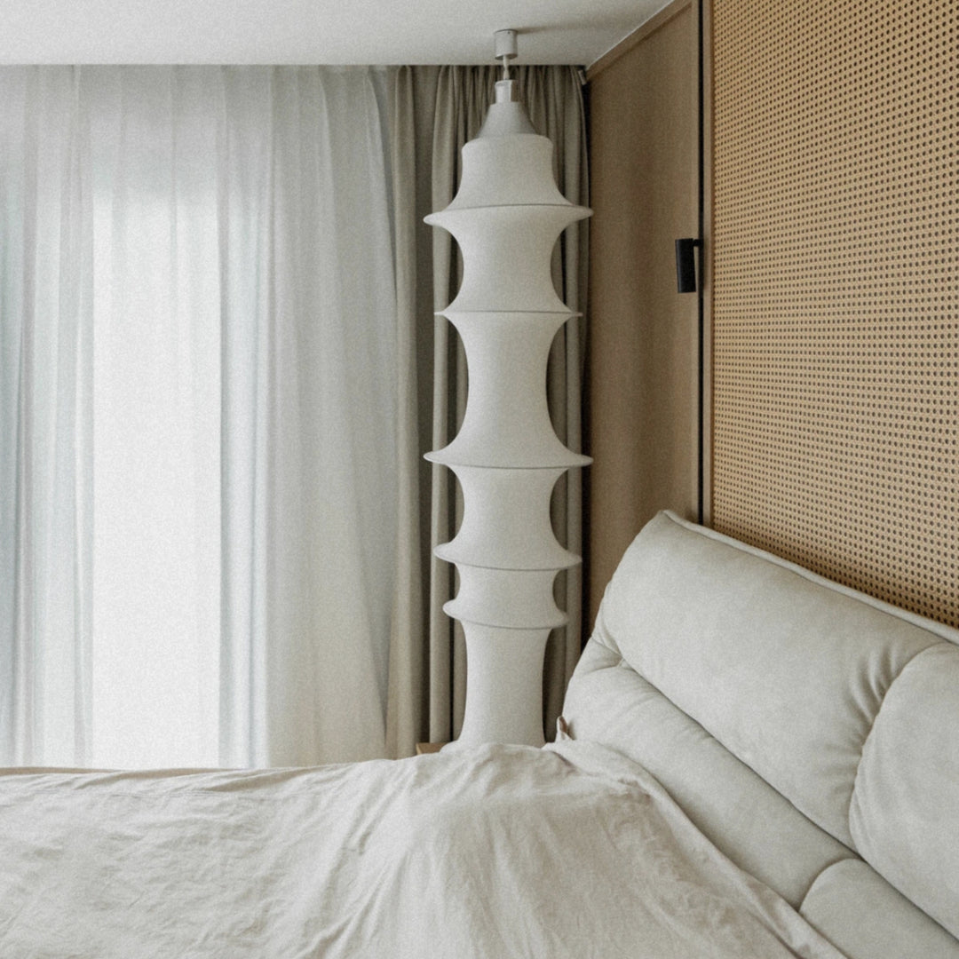 tall sculptural pendant light suspended beside a bed in a minimalist bedroom interior.