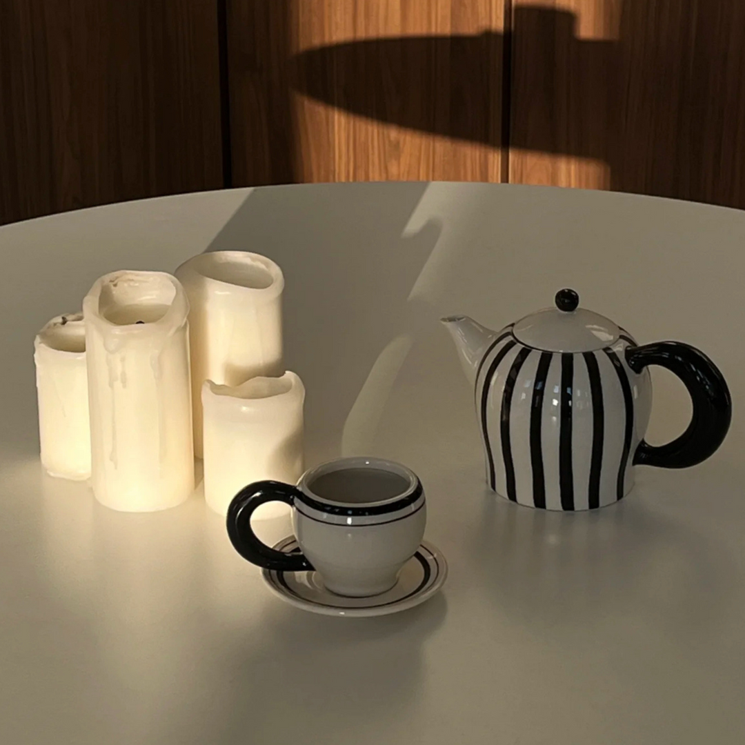 Tea set featuring teapot and small mug on modern table, illuminated by soft lighting.