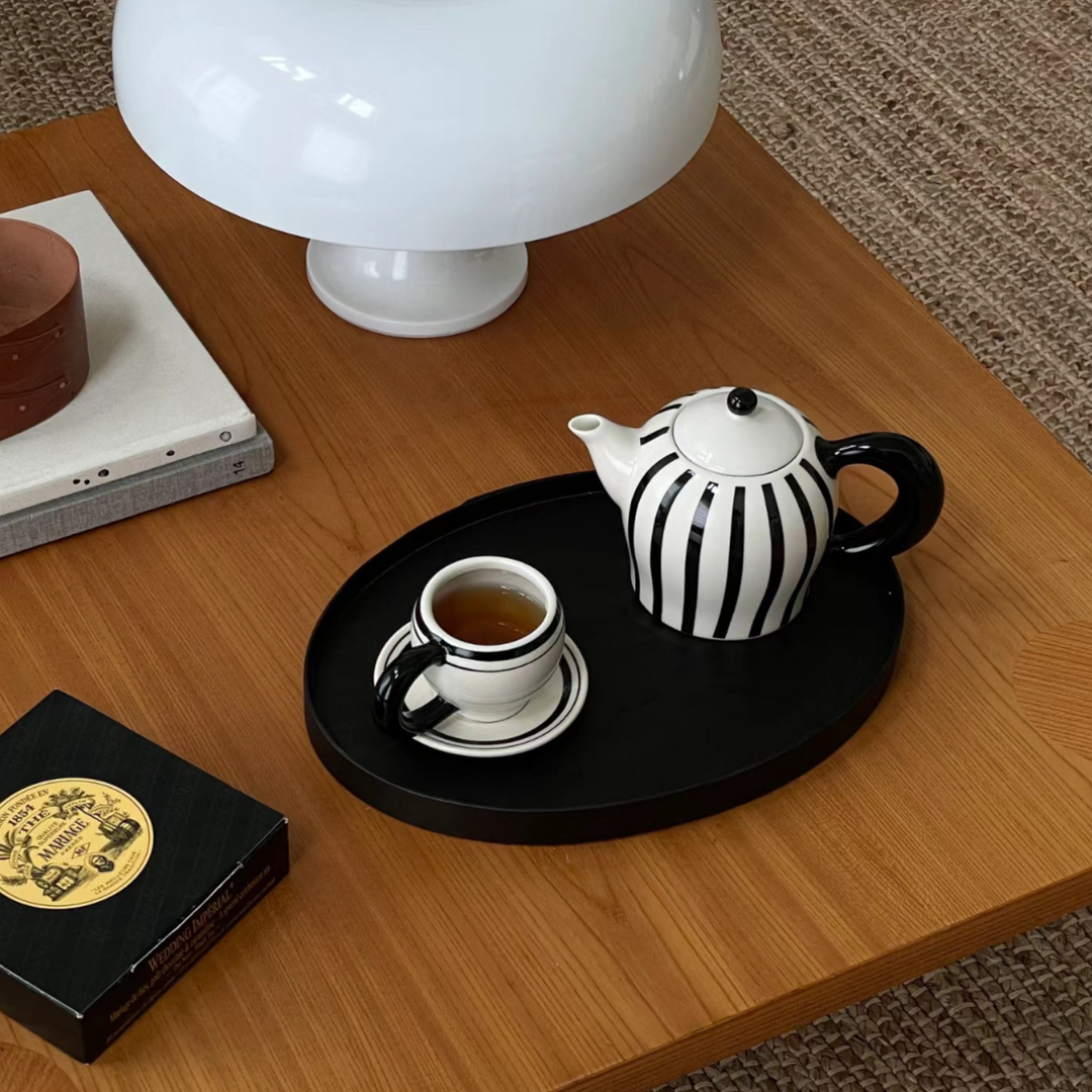 Teapot with small mug on a wooden table, featuring sleek black and white design.