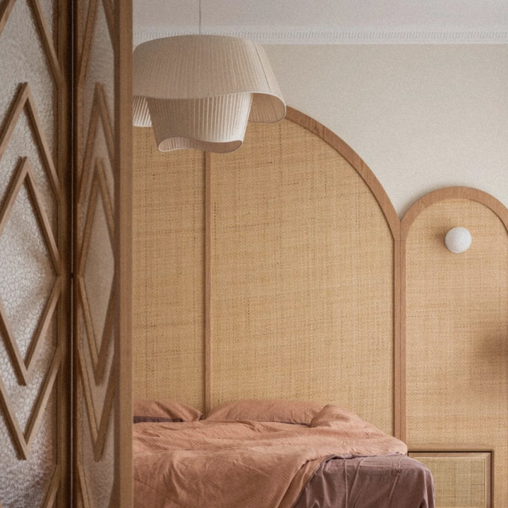 textile pendant light with layered fabric shade suspended above a bed in a calm bedroom interior.