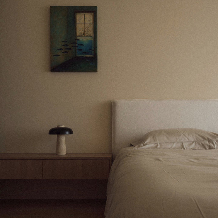 travertine bedside lamp placed on a wooden nightstand next to a neatly made bed.