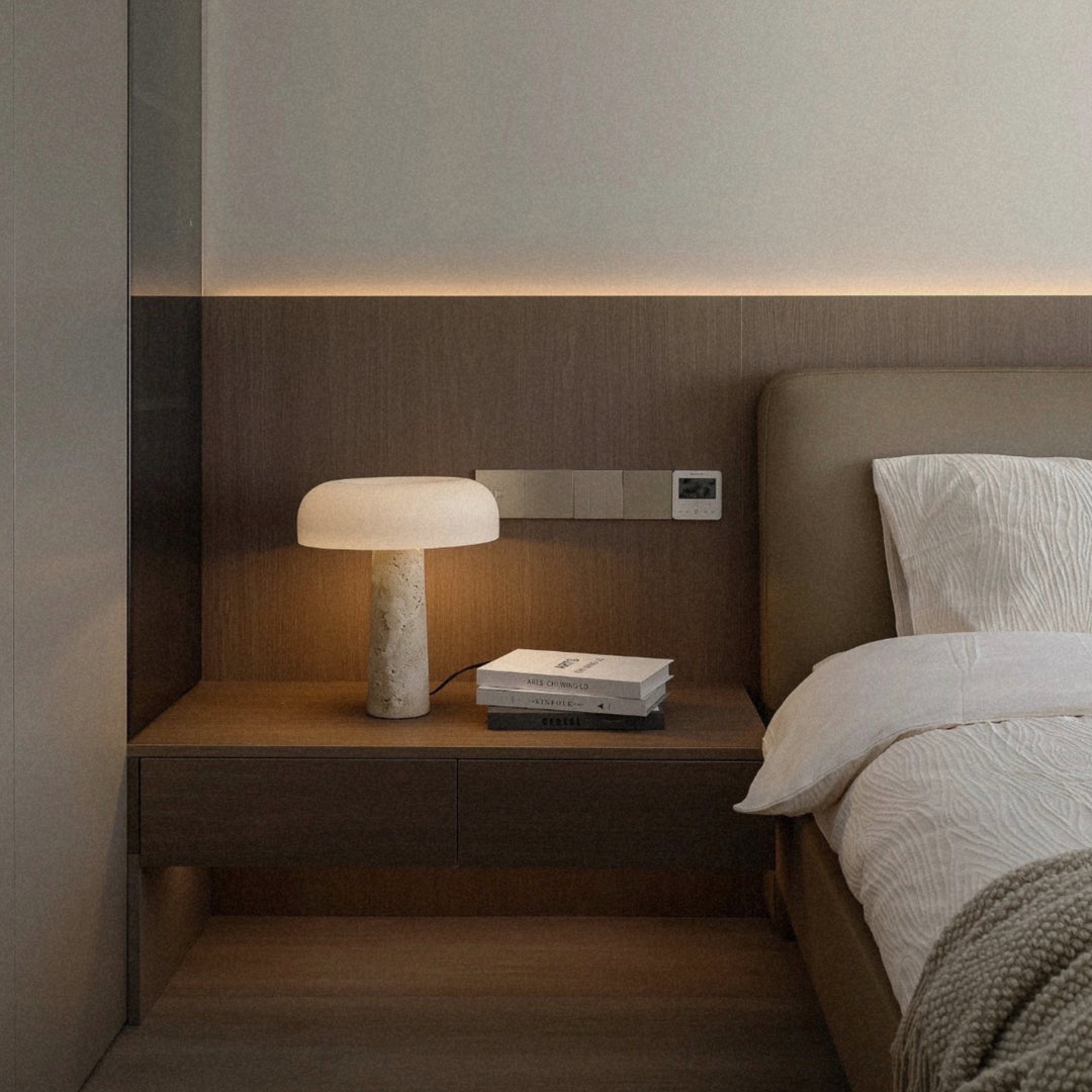 travertine stone bedside table lamp casting a warm glow on a built in nightstand in a calm modern bedroom.
