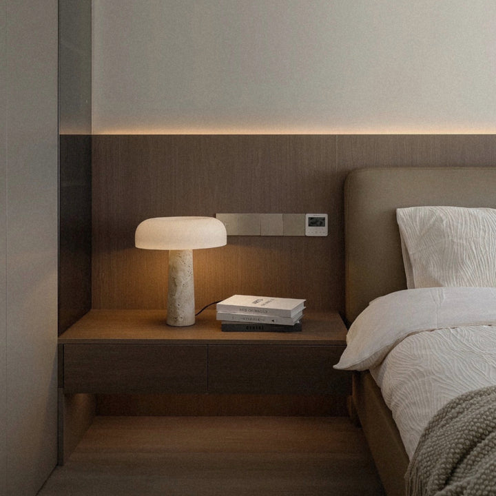 travertine stone bedside table lamp casting a warm glow on a built in nightstand in a calm modern bedroom.