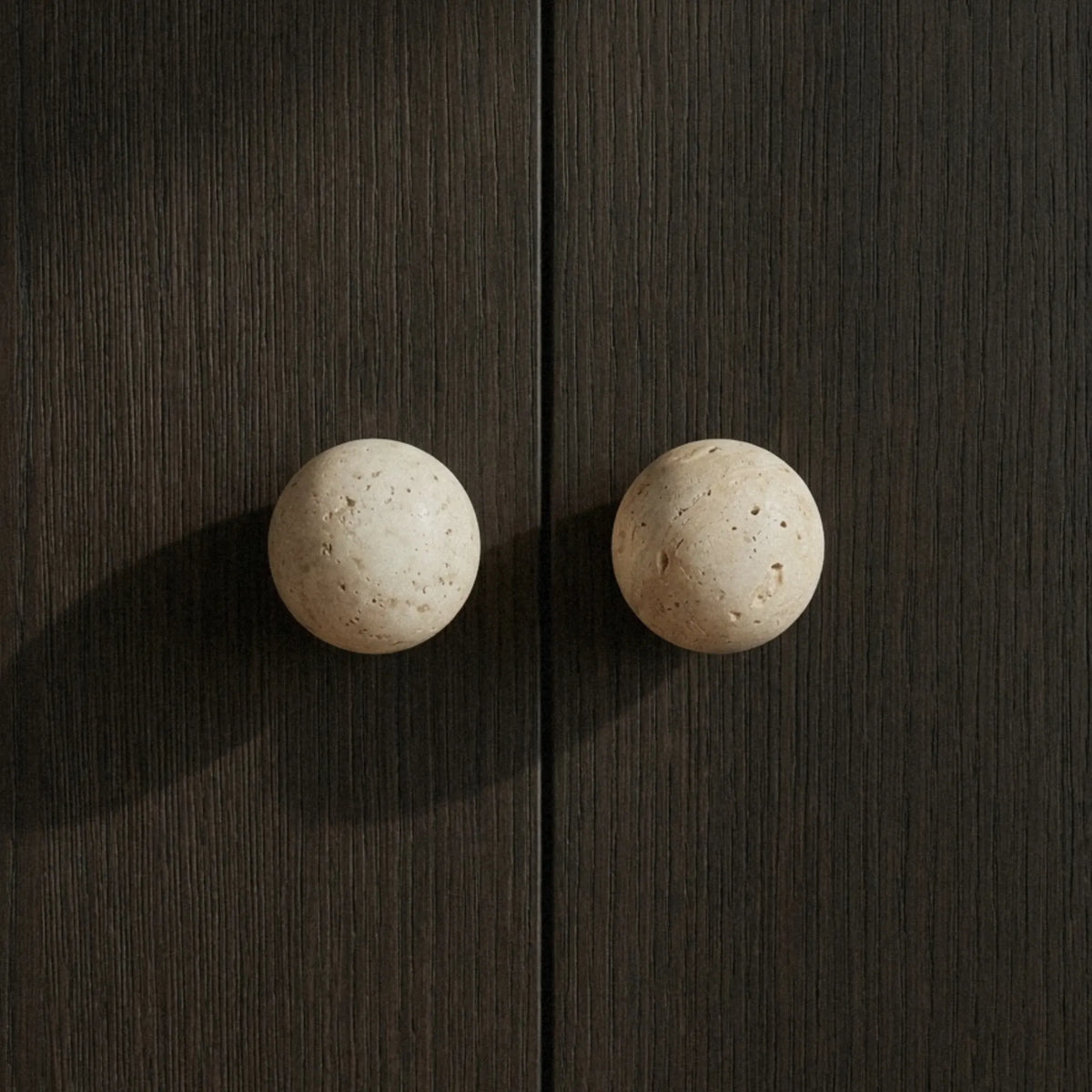 Paired travertine knobs on a dark oak cabinet warm stone texture against deep wood grain.