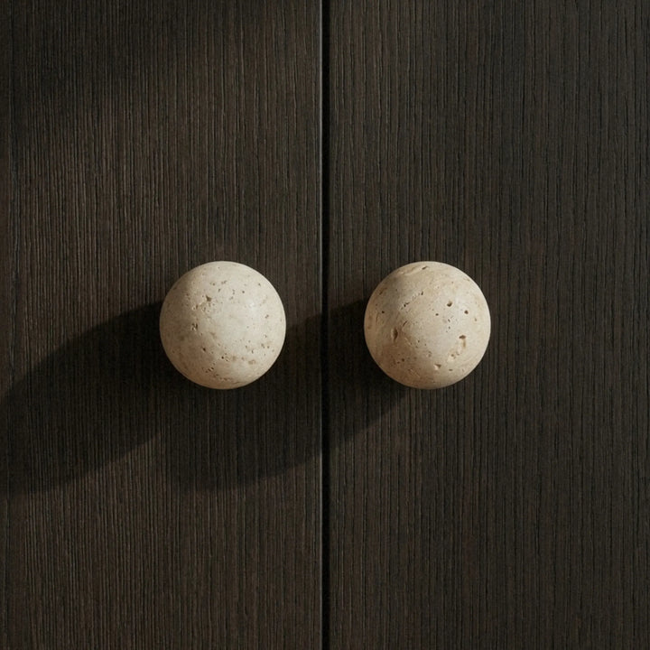 Paired travertine knobs on a dark oak cabinet warm stone texture against deep wood grain.