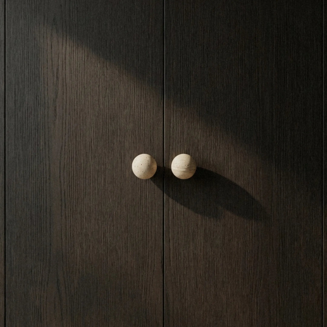Single travertine cabinet knob with a long soft shadow across dark wood quiet and precise.
