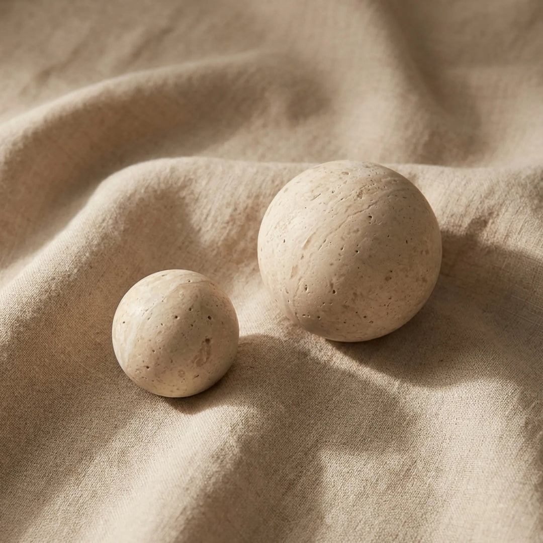 Travertine sphere cabinet knobs styled on soft linen fabric in organic modern decor.