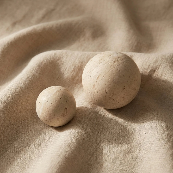 Travertine sphere cabinet knobs styled on soft linen fabric in organic modern decor.