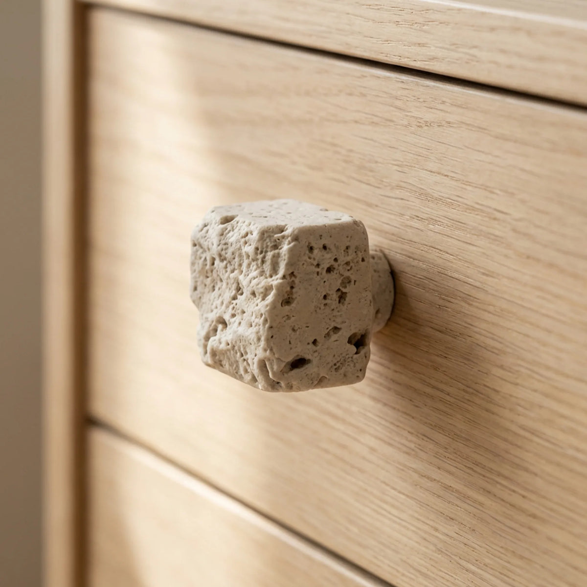 Travertine stone cabinet knob on light oak drawer in a neutral interior.
