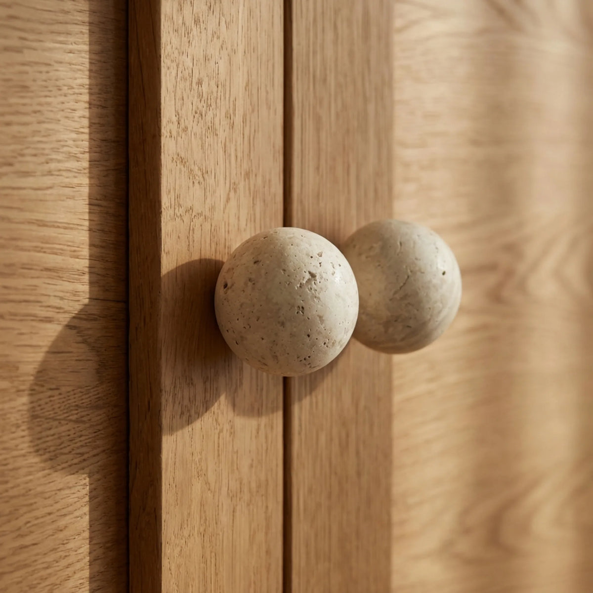 Travertine stone cabinet knobs on natural oak doors in a neutral modern interior.
