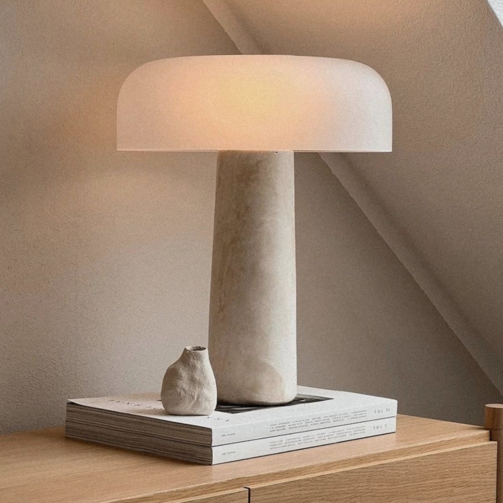 travertine stone table lamp with a sculptural base displayed on a wooden surface creating warm ambient light.