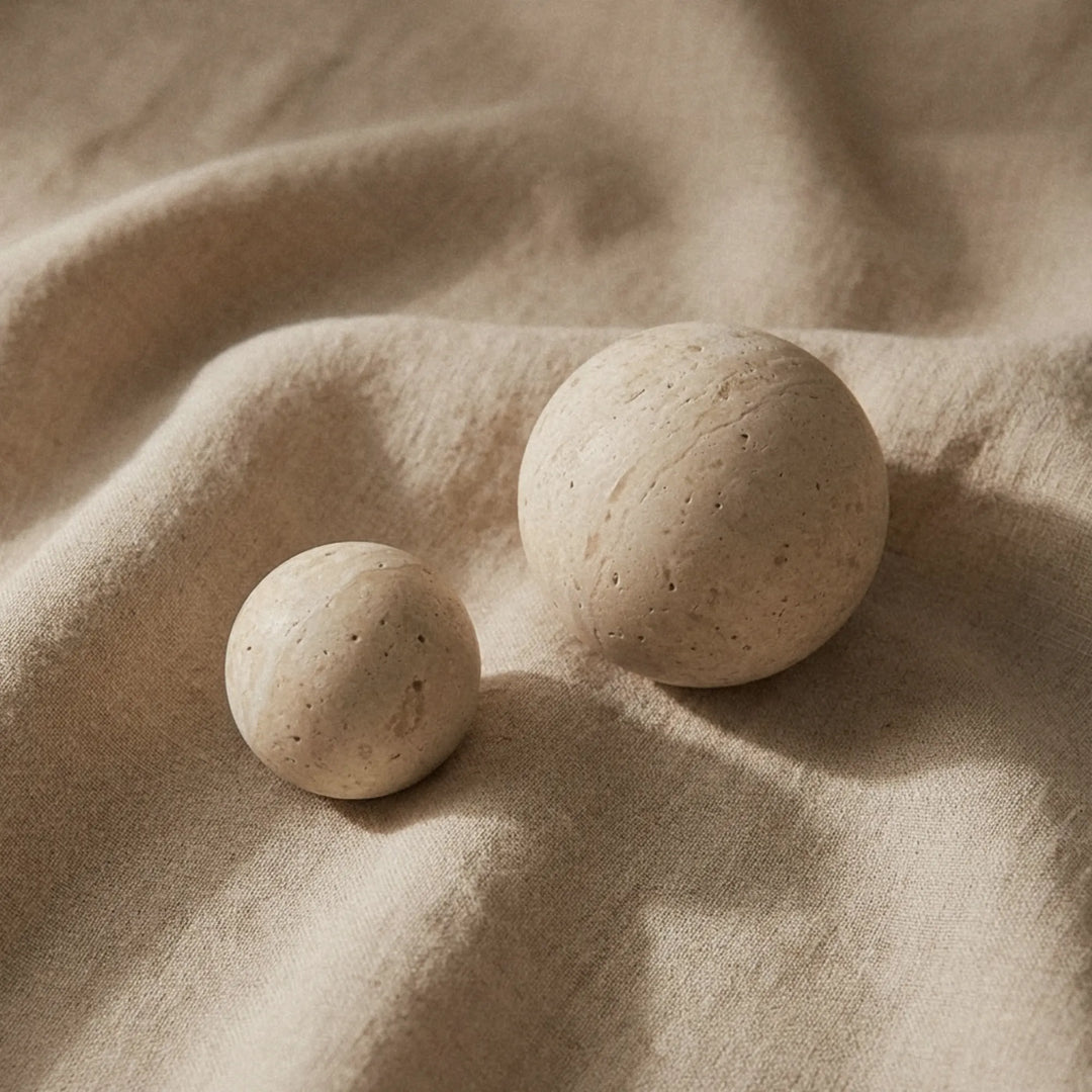 Two travertine knobs resting on folded linen, showing the natural speckled surface of the stone.