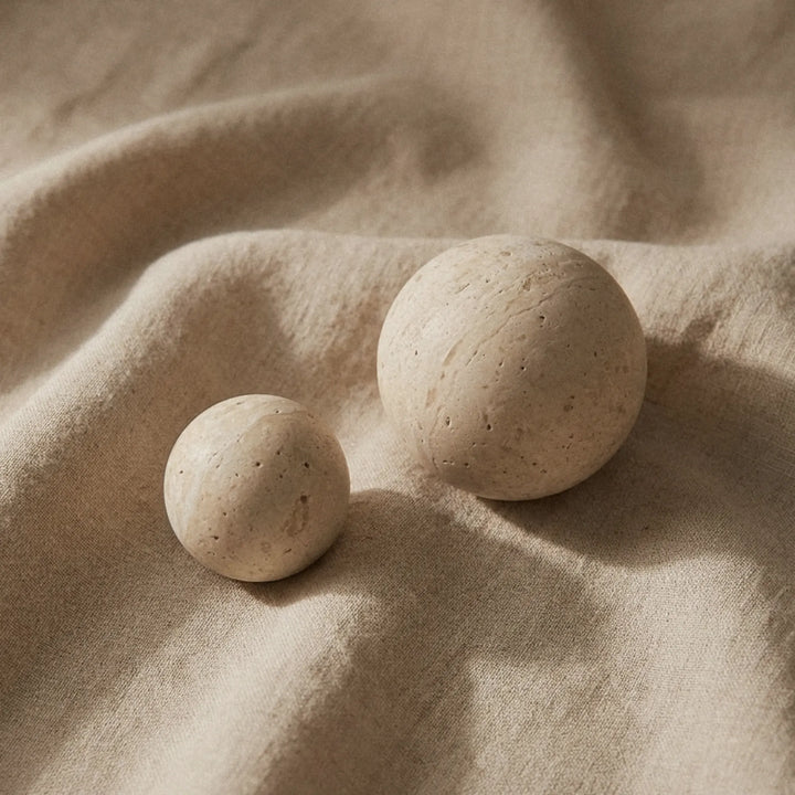 Two travertine knobs resting on folded linen, showing the natural speckled surface of the stone.