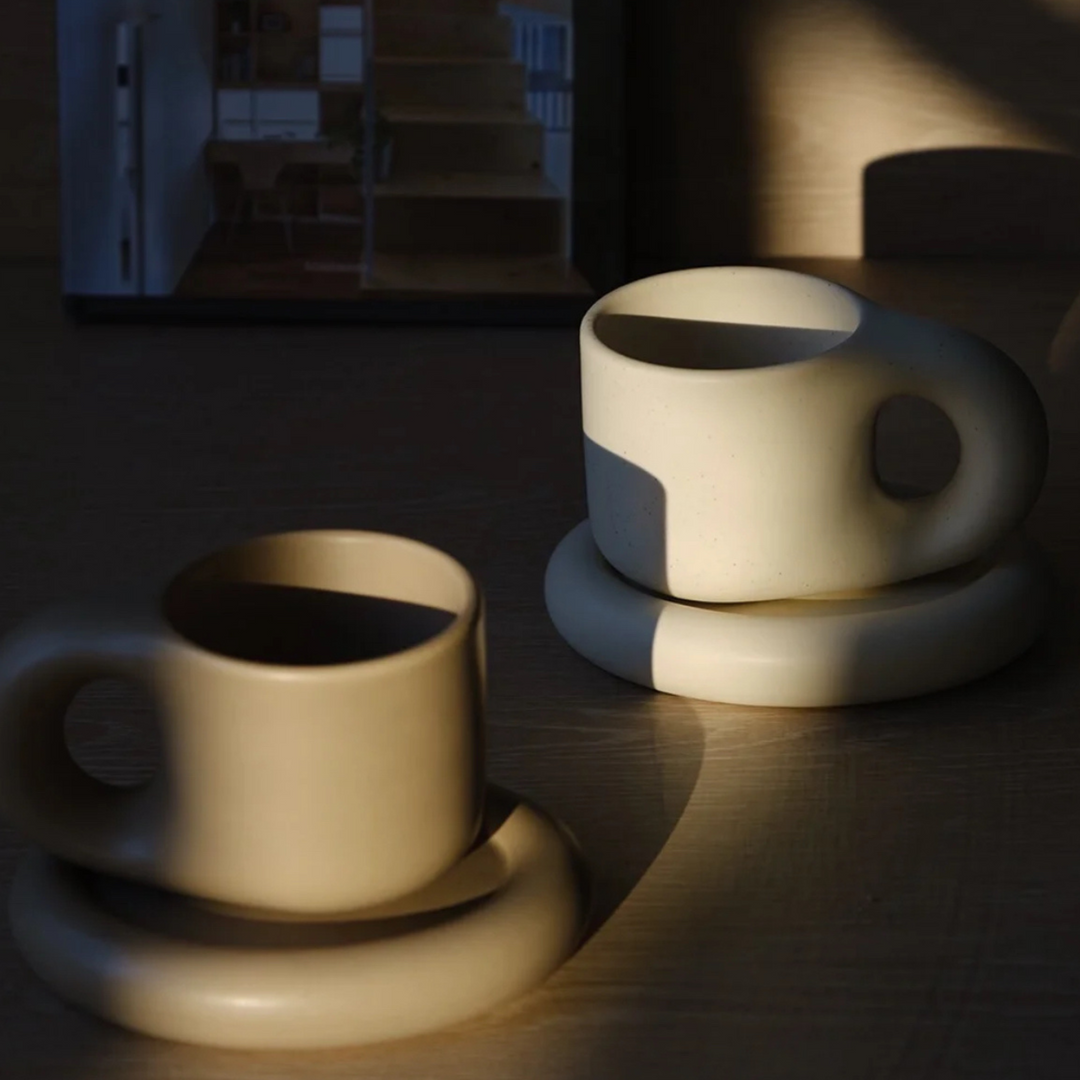 Chunky ceramic mug and plate set casting dramatic shadows in soft lighting.