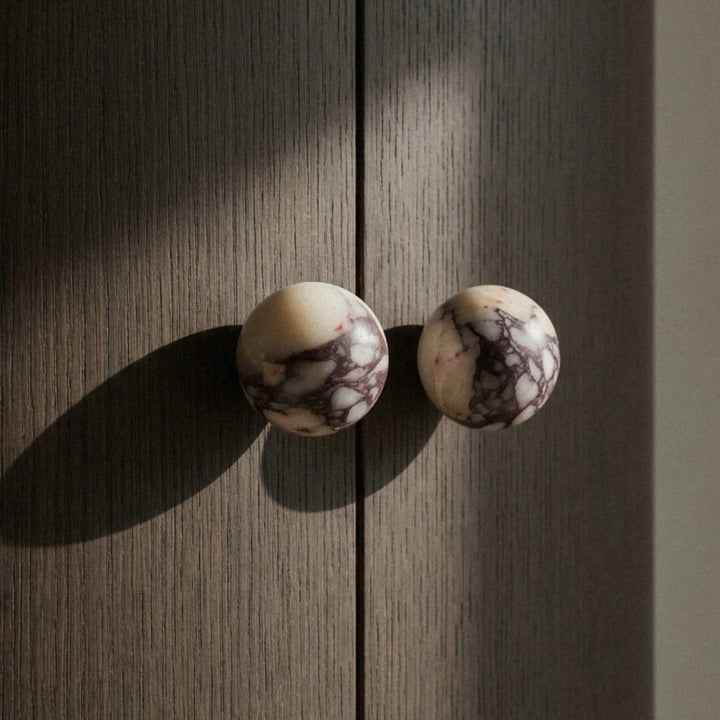 Calacatta Viola knobs catching directional light on a dark cabinet door, purple veins running across the cream stone.