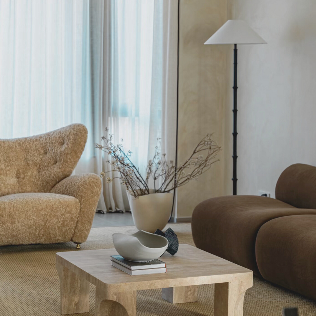 Handmade ceramic bowl in Wabi-Sabi-inspired living room with textured travertine table and earthy furniture.