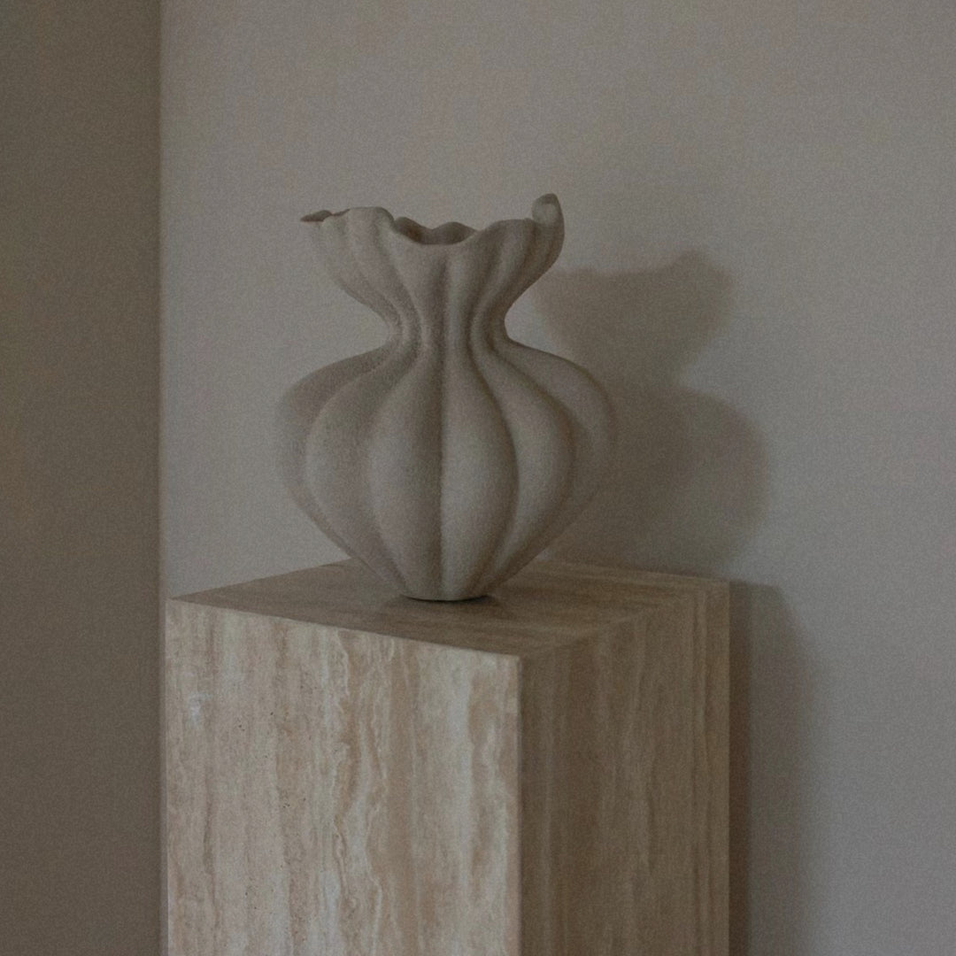 wabi sabi style sculptural ceramic vase displayed on a travertine pedestal with soft natural curves.