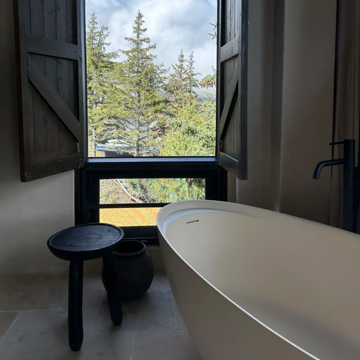 Dark wooden side table styled in a modern bathroom corner with a scenic window view.