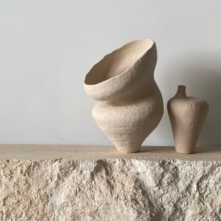 Wabi-sabi vase with uneven curves on textured stone surface.