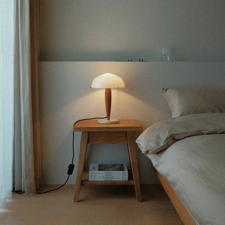 soft light from a walnut wood table lamp illuminates a bedside table in a calm bedroom interior.