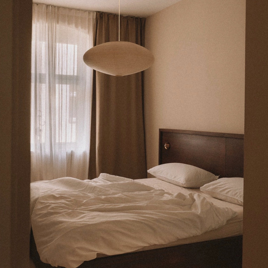 washi paper ceiling lamp floating above a bed in a warm minimalist bedroom.