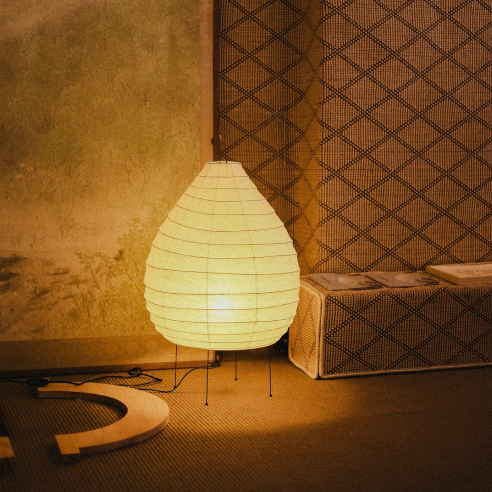 washi paper floor lamp emitting a warm ambient glow placed beside a textured wall in a calm modern interior.