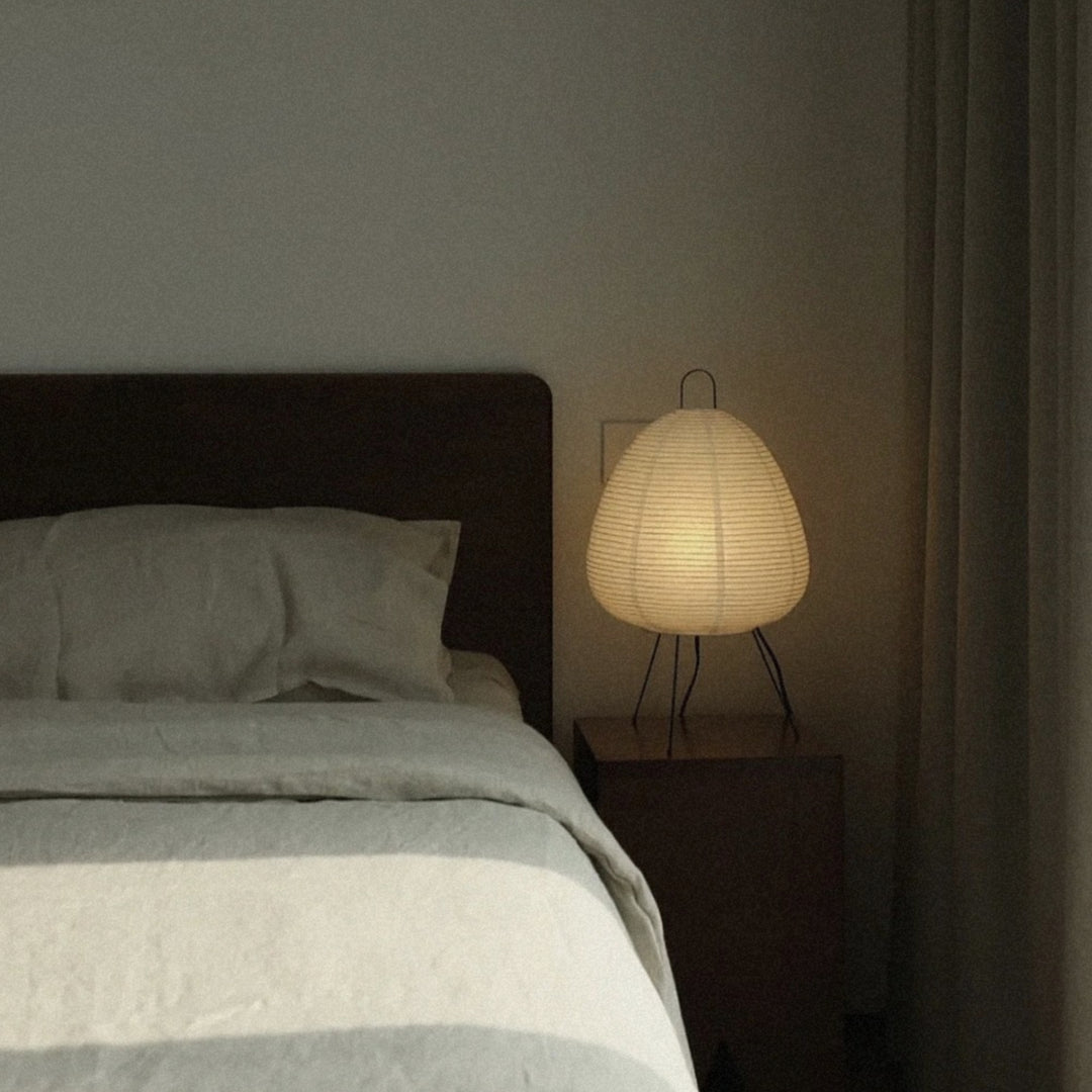 soft glow from a washi paper table lamp sits beside the bed in a quiet bedroom corner.