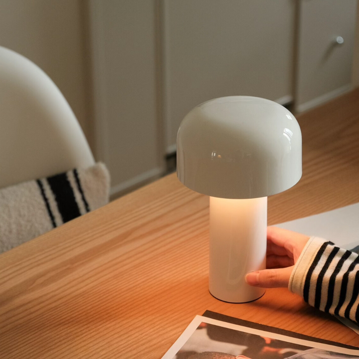 A white cordless mushroom lamp glowing on a wooden desk with a cozy setting.