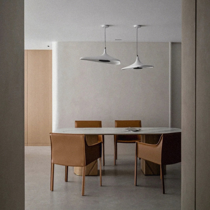 white modern pendant light hanging above a dining table in a bright minimalist dining room.